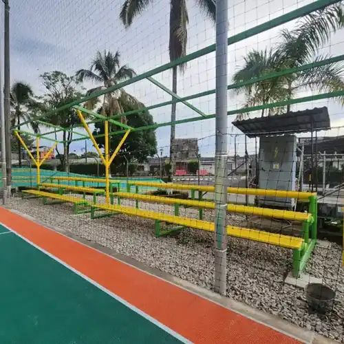 Estructura metálica y cerramiento de malla para cancha sintética de fútbol. Se aprecian bancas de suplentes en colores amarillo y verde, instalación profesional Gapac.